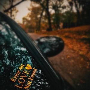 May include: A black car window with a gold sticker that reads "Error 404 Love Not Found" with a broken heart icon.