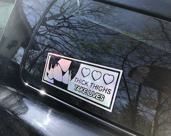 May include: A silver sticker with a black silhouette of a person's lower body and the text "THICK THIGHS TAKE LIVES" with three pink hearts above the text.