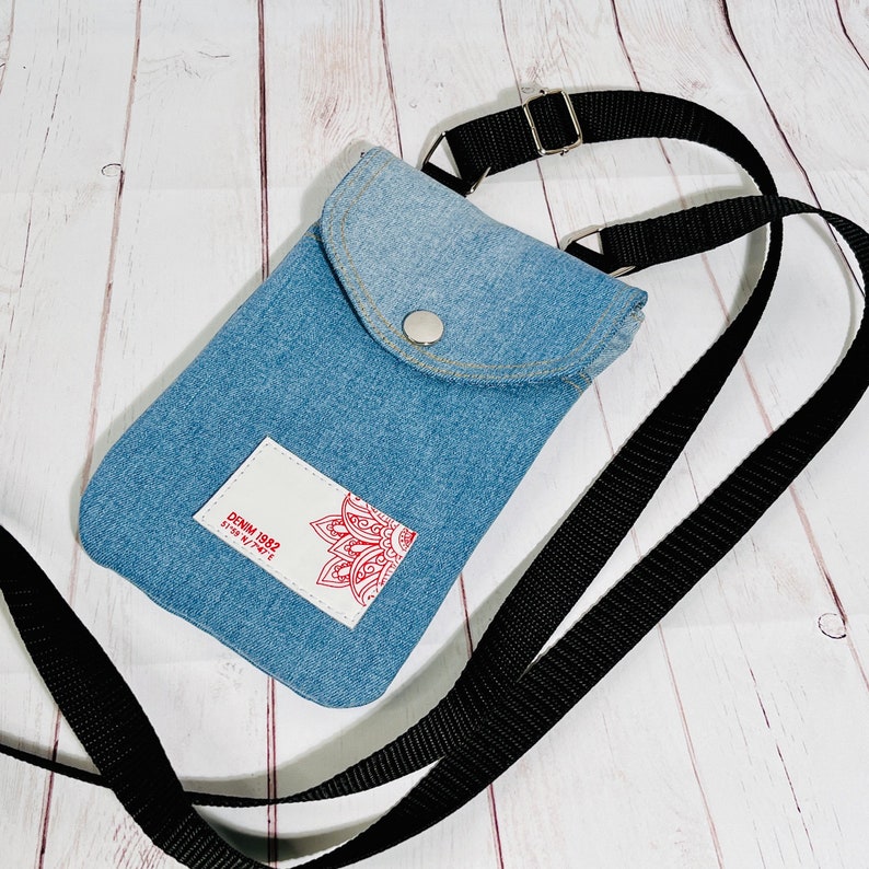 crossbody tasche umhängetasche aus hellblauer upcycling jeans, smartphonetasche zum umhängen, vorderansicht liegend