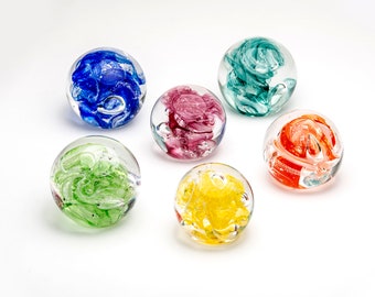 May include: Six glass paperweights with swirls of colour inside. The paperweights are in shades of blue, green, pink, orange, yellow, and green.