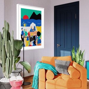 May include: A framed wall art print featuring a colorful abstract illustration of a beach scene with a red sun, blue water, black mountains, and stylized figures. The artwork is displayed in a white frame hanging on a light purple wall above an orange armchair.