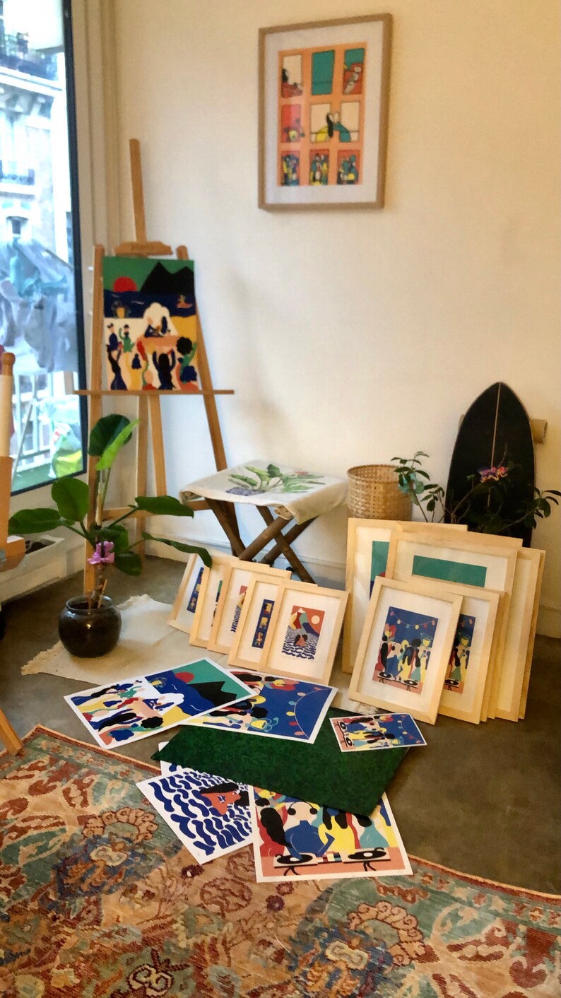 K&ouml;nnte beinhalten: Eine Sammlung gerahmter und ungerahmter Kunstdrucke mit farbenfrohen, stilisierten Illustrationen von Menschen in verschiedenen Umgebungen, die auf einer Staffelei, einem Hocker und dem Boden neben einer Topfpflanze und einem dunklen Objekt stehen.