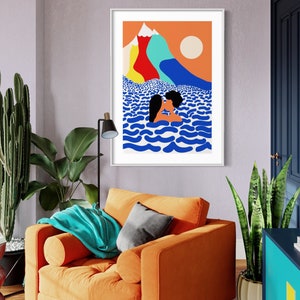 May include: A framed wall art print featuring a colorful illustration of two figures kissing in blue wavy water. The background displays a bright orange sky, a pale sun, and stylized mountains in shades of yellow, red, light blue, and white.