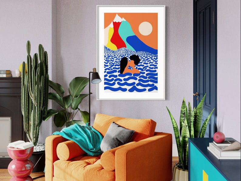 May include: A framed wall art print featuring a colorful illustration of two figures kissing in blue wavy water. The background displays a bright orange sky, a pale sun, and stylized mountains in shades of yellow, red, light blue, and white.