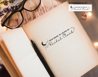 May include: A close-up of a book with a black and white moon and stars design stamped on the page. The stamp reads "This book is loved by Rachel Clark".
