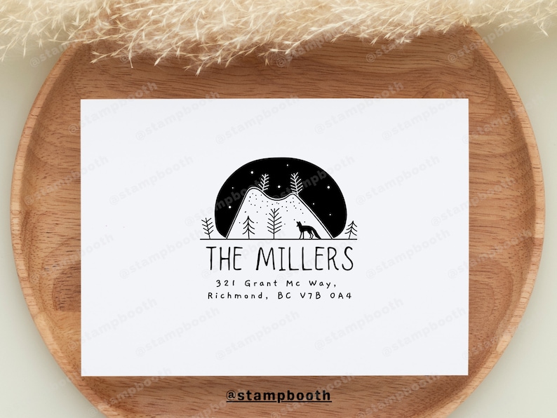 May include: A black and white illustration of a mountain range with a fox silhouette in front of a crescent moon. The text "THE MILLERS" is below the image, followed by the address "321 Grant Mc Way, Richmond, BC V7B 0A4". The text "@stampbooth" is at the bottom of the image.