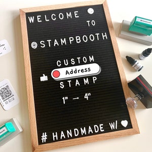May include: A black letter board with white letters spelling "WELCOME TO @STAMPBOOTH CUSTOM Address STAMP 1" - 4" #HANDMADE W/" with a red circle and a thumbs up icon. There are several green and black ink pads and ink bottles on a white surface.