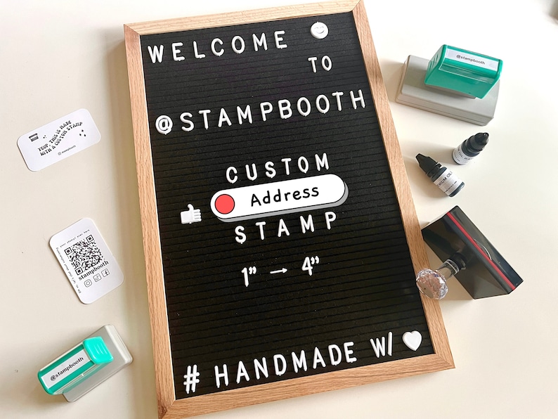 May include: A black letter board with white letters spelling "WELCOME TO @STAMPBOOTH CUSTOM Address STAMP 1" - 4" #HANDMADE W/" with a red circle and a thumbs up icon. There are several green and black ink pads and ink bottles on a white surface.