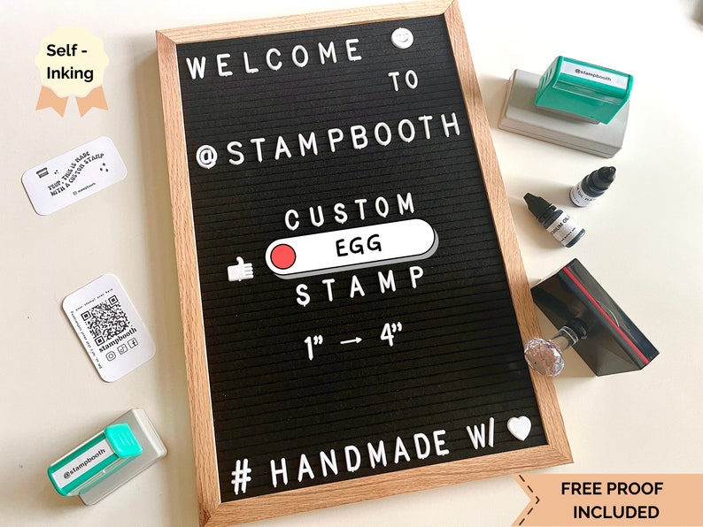 May include: A black letter board with the text "WELCOME TO @STAMPBOOTH CUSTOM EGG STAMP 1" - 4" #HANDMADE W/" and a white heart. The board is surrounded by various craft supplies, including ink pads, ink bottles, and a self-inking stamp.