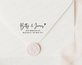 May include: A white envelope with the names "Betty & James" in elegant black script, a small heart symbol, and an address. A pink wax seal with a leaf design is at the bottom. The envelope is on a white surface.