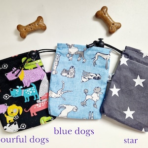 May include: Three fabric drawstring pouches with black cords and toggles. The left pouch is black with colourful dog illustrations, the centre pouch is light blue with various dog breeds, and the right pouch is dark grey with white stars.