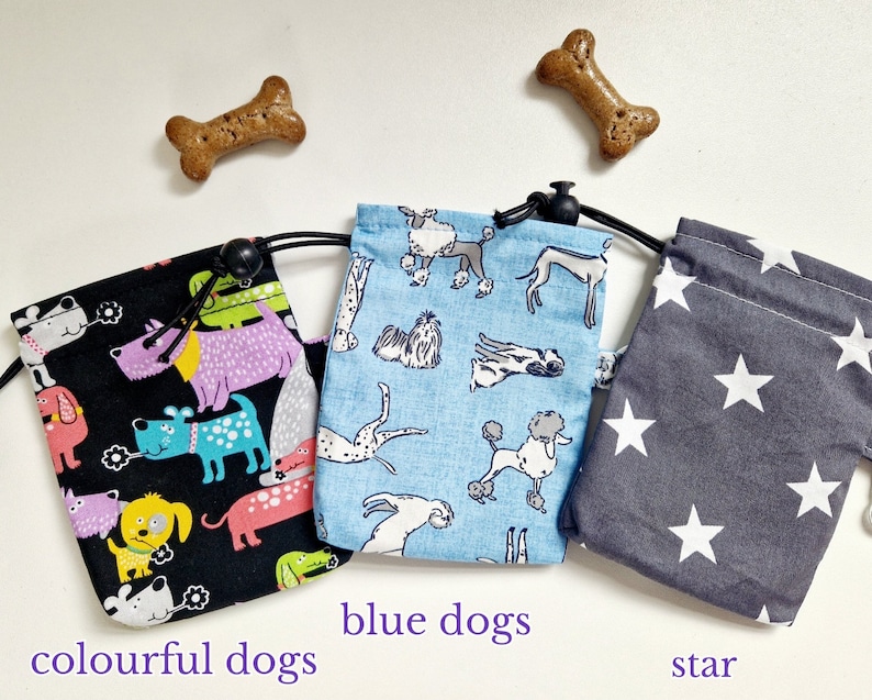 May include: Three fabric drawstring pouches with black cords and toggles. The left pouch is black with colourful dog illustrations, the centre pouch is light blue with various dog breeds, and the right pouch is dark grey with white stars.