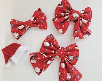 May include: Three red fabric bows featuring a repeating pattern of Santa Claus figures, wrapped gifts, and small white stars, accompanied by a miniature red and white felt Santa hat with a white pom-pom at the tip.