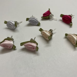 May include: Assortment of six pairs of rose-shaped earrings. The earrings are made of fabric and have a silver post. The roses are in shades of pink, white, and red.