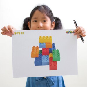 May include: A child is holding up a white sheet of paper with a colourful drawing of a tower made of toy building blocks. The paper has the words "2D TO 3D" printed at the top and the words "TOY 4 PLAY" printed at the bottom.