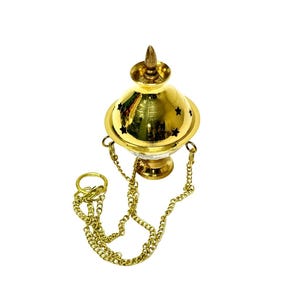 May include: A gold-colored incense burner with a star-shaped pattern and a conical top. The burner is suspended by a gold chain and ring. The design is ornate and reflective, suggesting a decorative or ceremonial purpose.