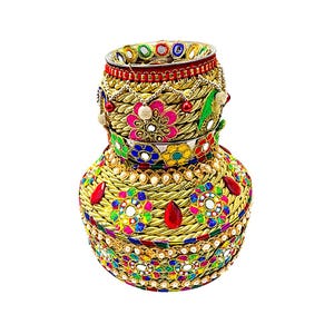 May include: An ornate, decorative pot with a gold-colored woven exterior. The pot is adorned with colorful floral patterns, red jewels, and mirrored accents. The rim is lined with a red band and small, colorful mirrors. The overall design is intricate and eye-catching.