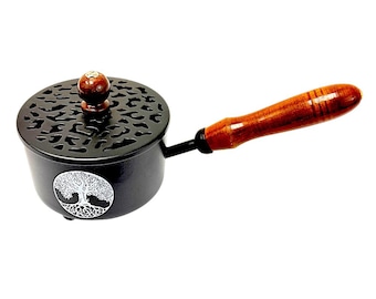 May include: A black metal incense burner with a long wooden handle and a round lid featuring a cutout pattern. The side of the burner displays a white circular emblem of a tree with visible roots. A small wooden knob sits atop the lid.