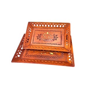 May include: Two rectangular wooden serving trays with intricate floral and geometric cut-out designs. The trays are a warm brown color with gold accents and feature carved details, including an elephant motif.