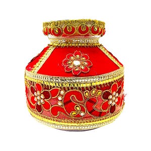 May include: A red decorative pot with gold trim and floral embellishments. The pot features a wide base that tapers to a narrower opening, with intricate gold detailing around the rim and base. The floral designs are accented with small, white embellishments.