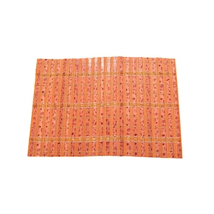 May include: Orange bamboo placemat with a floral pattern. The placemat is rectangular and made of vertical bamboo strips held together with horizontal strips. The floral pattern is a darker shade of orange.