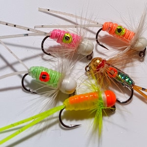 May include: Assortment of six colorful fishing lures with white, orange, green, and yellow accents. The lures have different colored bodies and feathers.