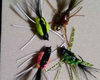 May include: Four different fly fishing lures with black, green, red, and yellow accents. The lures have long tails and are tied with feathers and other materials.