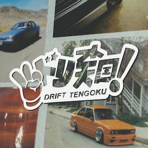 May include: White sticker with a hand making a peace sign, Japanese text, and the words "Drift Tengoku". The sticker is on a background of a photo of a car.