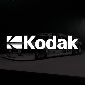 Peut inclure: Une voiture de course blanche arborant le logo Kodak et le numéro 24 sur le côté. Le véhicule présente divers autocollants de sponsors, dont Avon, Bosch et Shell, avec un aileron avant bas et des roues de course détaillées à rayons multiples.