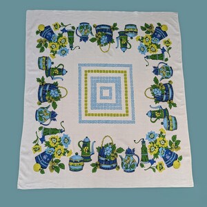 May include: White tablecloth with a repeating pattern of blue and green teapots, pitchers, and floral arrangements. A square geometric design in blue and green is in the center. The tablecloth is likely vintage.