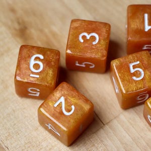 Può includere: Sei dadi dorati con numeri bianchi. I dadi sono sparsi su una superficie di legno. I numeri sui dadi sono 1, 2, 3, 4, 5 e 6.