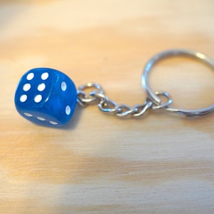 Peut inclure: Un porte-clés avec un dé bleu et des points blancs. Le dé est attaché à une chaîne et un porte-clés argentés. Ce porte-clés est un accessoire amusant, idéal pour les amateurs de jeux.