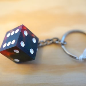 May include: A multi-colored dice keychain with white dots. The dice is attached to a silver chain and keyring. The dice has a marbled appearance with colors of red, green, and blue.