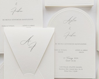 May include: Elegant white wedding invitations with arched and rectangular designs. The invitations feature the names "Aylin & Furkan" in cursive script, along with event details. A matching envelope with initials is also present.