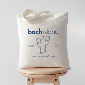 Puede incluir: Una bolsa de lona blanca con un dise&ntilde;o azul y rosa. La bolsa dice "bach island" con un coraz&oacute;n y dos copas de champ&aacute;n. El texto "Turks and Caicos" y "March 2024" tambi&eacute;n est&aacute;n en la bolsa. El texto "Jenna's Bachelorette" est&aacute; en la parte inferior de la bolsa.