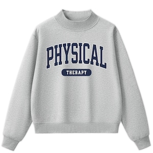 May include: A light gray long-sleeve sweatshirt with a mock neck collar. The front features the dark blue text PHYSICAL in an arched collegiate font, with the word THERAPY printed in a smaller, bold font inside a dark blue horizontal pill shape.