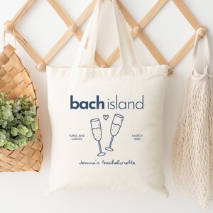 Puede incluir: Bolsa de lona blanca con el texto "bach island" en azul, un coraz&oacute;n rosa y dos copas de champ&aacute;n brindando. El texto "Turks and Caicos" y "March 2024" tambi&eacute;n est&aacute;n impresos en la bolsa. La bolsa dice "Jenna's Bachelorette" en la parte inferior.