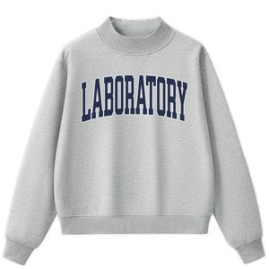 May include: A light gray long-sleeve sweatshirt with a mock neck collar. The front features the word LABORATORY printed in a dark navy blue collegiate-style font. The garment has ribbed cuffs and a ribbed hem, providing a structured fit.