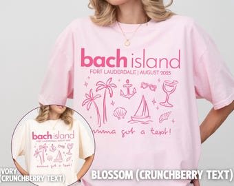May include: Two pink t-shirts with the text "bach island" and "Fort Lauderdale | August 2025" printed on them. The shirts have a pink graphic of palm trees, a sailboat, an anchor, seashells, and a cocktail glass. The text "wanna get a text!" is printed below the graphic. One shirt is ivory with crunchberry text and the other is blossom with crunchberry text.