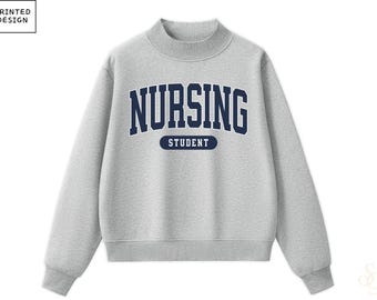 May include: A heather grey long-sleeve sweatshirt with a mock neck collar. The front features the dark blue text NURSING in a collegiate font, with the word STUDENT printed in white inside a dark blue horizontal pill-shaped graphic below it.