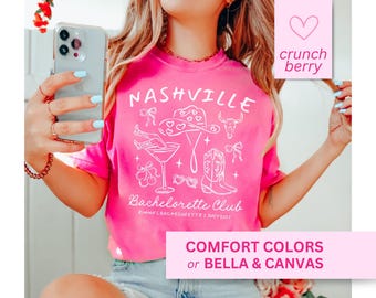 May include: Pink t-shirt with a white graphic design that says "Nashville Bachelorette Club" with a cowboy hat, boots, and a martini glass. The text "Emma's Bachelorette | July 2023" is also on the shirt.