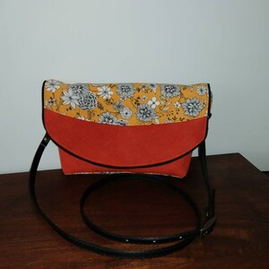 Peut inclure: Sac à bandoulière avec rabat à motifs floraux jaunes et blancs et corps rouge. Le sac a une bandoulière et une bordure noires. Le sac est conçu avec un rabat incurvé et un corps rectangulaire.
