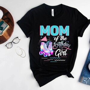 Może przedstawiać: Czarny T-shirt z napisem "MOM of the Birthday Girl" w kolorze niebieskim i r&oacute;żowym. Projekt zawiera parę r&oacute;żowych i niebieskich rolek z tęczowymi akcentami.