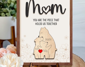 May include: Wooden sign with the word "Mom" and a heart in the middle. The sign says "You are the piece that holds us together." Below the text is a wooden cutout of three bears hugging. The bears are labeled "Jennifer", "Ralph", and "Philip".