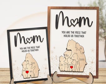 May include: Two wooden signs with the word "Mom" and a heart in the center. The signs feature a family of bears with the names of each family member written on them. The text on the signs reads "You are the piece that holds us together."