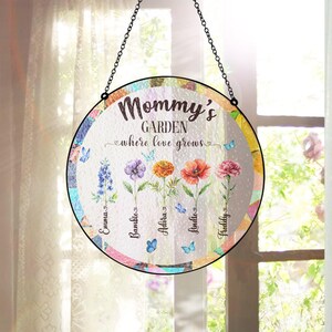 Puede incluir: Un letrero redondo de vidrio con un diseño floral colorido y el texto "Mommy's Garden where love grows". El letrero tiene cinco flores con nombres escritos debajo de cada flor: Emma, Bambie, Altera, Lindie y Freddy.