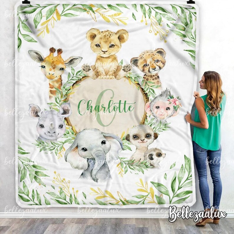 May include: A white baby blanket with a green and yellow leafy border. The centre features a circle with the name "Charlotte" in green lettering.  Surrounding the circle are various animal illustrations, including a giraffe, lion, elephant, rhino, monkey, and meerkat.