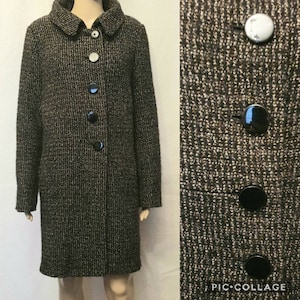 May include: A long, textured coat in shades of brown, black, and white. The coat has a rounded collar and is fastened with five buttons. The buttons are a mix of black and silver. The coat's fabric has a woven appearance.