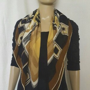 May include: A square scarf with a geometric pattern in black, brown, white, and yellow. The scarf is draped around a mannequin's neck, showcasing its design. The scarf's edges are trimmed with a brown border.