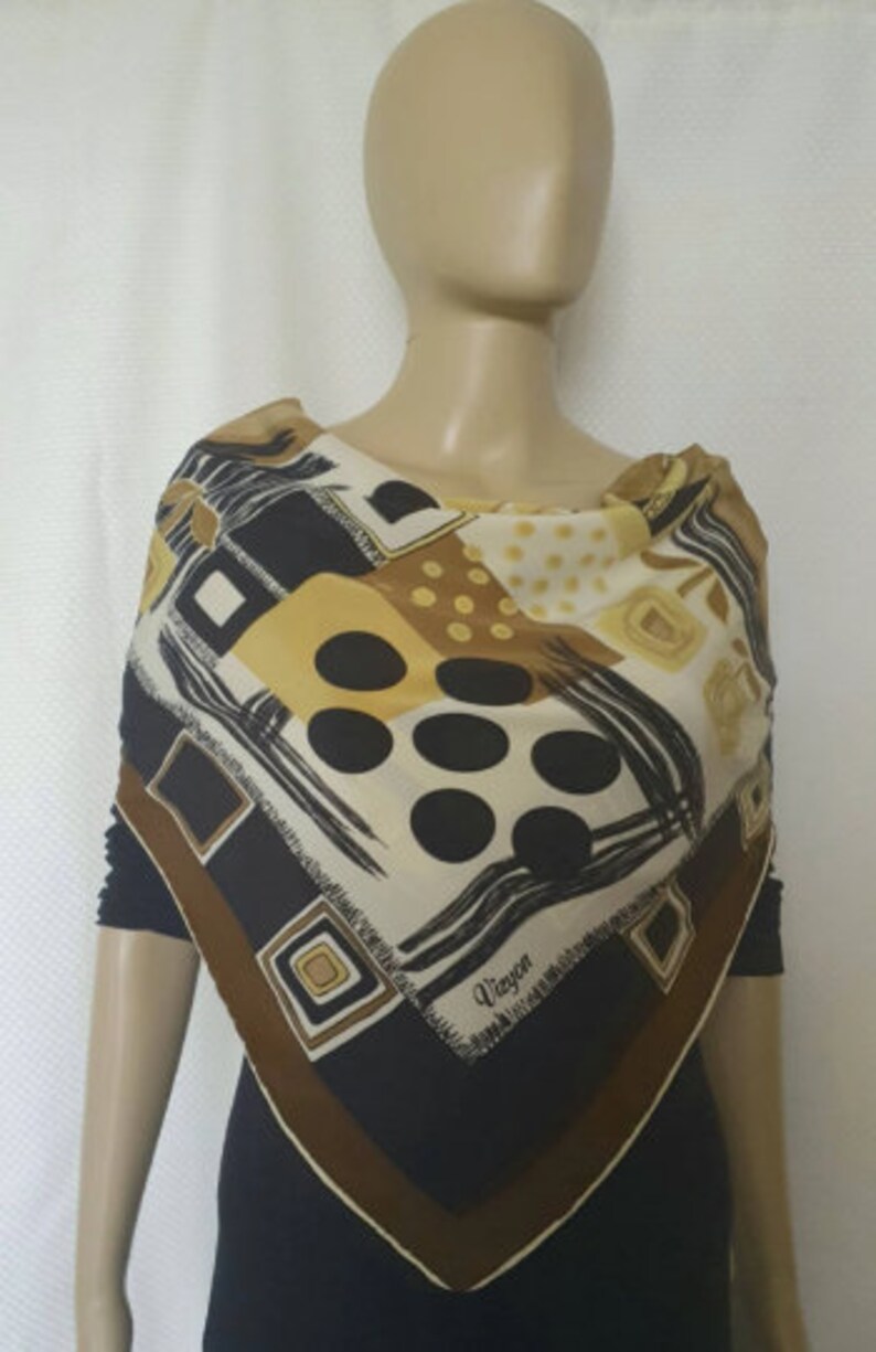 May include: A square silk scarf with a geometric pattern in black, brown, cream, and gold. The scarf features squares, circles, and brushstroke designs. The word "Vieyon" is printed on the scarf.